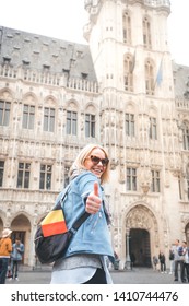 Young happy cheerful woman in a blue jacket showing thumb up against the backdrop of the Grand Place in Brussels, Belgium
