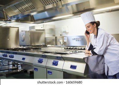 Young happy chef standing next to work surface phoning in professional kitchen - Powered by Shutterstock