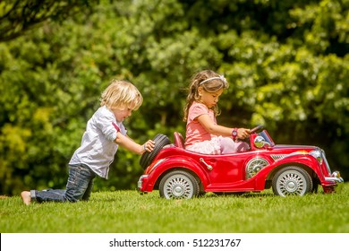young happy children - boy and girl - driving a toy car outdoors in park