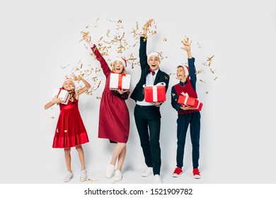 A Young Happy Christmas Family With Children Dressed In Santa Hats Is Having Fun With Christmas Gifts In Hand, Tossing Confetti On A White Background. New Year, Christmas, Holiday