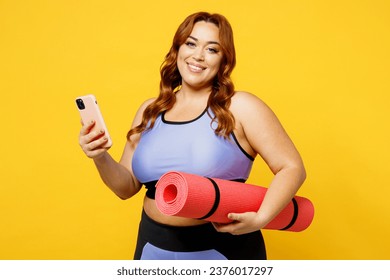 Young happy chubby overweight plus size big fat fit woman wear blue top warm up training hold yoga mat use mobile cell phone isolated on plain yellow background studio home gym. Workout sport concept - Powered by Shutterstock