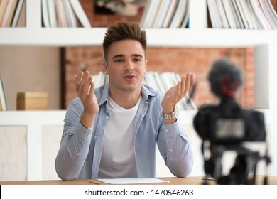 Young Happy Confident Cool Male Student Sitting At Table In Front Of Camera, Recording Self-introduction Video For Scholarship Or Educational Grant Achievement. Millennial Guy Sharing Studying Tips.