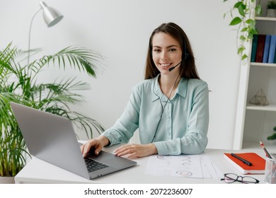 Young Happy Confident Employee Operator Business Woman In Set Microphone Headset Blue Shirt For Helpline Assistance Sit Work At Call Center Workplace Desk With Laptop Pc Computer Typing Office Indoors