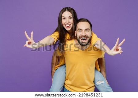 Young happy cool couple two friends family man woman together wear yellow casual clothes giving piggyback ride to joyful, sit on back show v-sign isolated on plain violet background studio portrait.