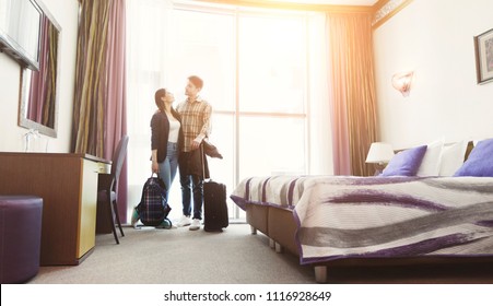 Young happy couple arrived to hotel room on honeymoon. Family standing on window background - Powered by Shutterstock