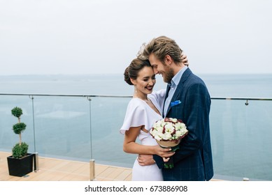 young happy couple of bride and groom stand embracing on the balcony near the sea