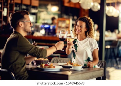 Young happy couple celebrating and toasting with wineglasses while eating in a restaurant. 