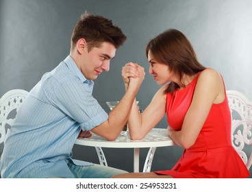 Young happy couple challenge fighting in arm-wrestling at table, in studio isolated on gray