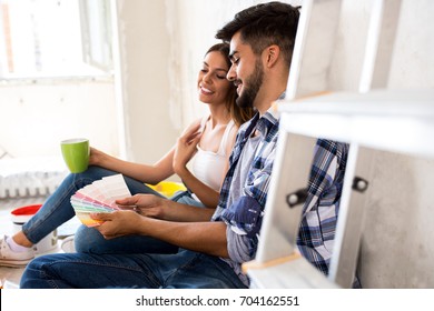 Young happy couple choosing colors for painting their home while doing break and drinking coffee
