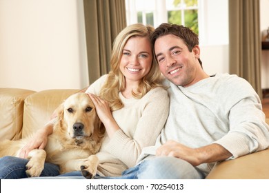 Young Happy Couple With Dog Sitting On Sofa