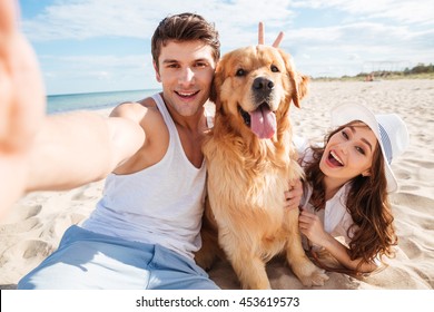 Young happy couple with dog taking a selfie at the beach - Powered by Shutterstock