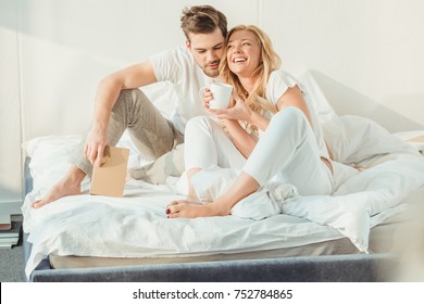 young happy couple drinking coffee in bed at morning