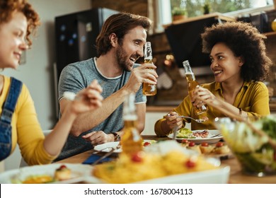 Young happy couple eating with friends at dining table and toasting with beer bottles. 