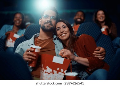 Young happy couple eating popcorn while watching movie in cinema. - Powered by Shutterstock