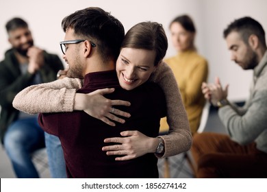 Young Happy Couple Embracing While Taking A Part In Group Therapy At Community Center. 
