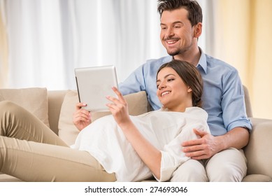 Young happy couple expecting a baby. They are using a tablet. - Powered by Shutterstock