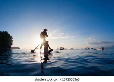 Young happy couple have fun on stand up paddleboard. Active paddle boarder paddling by sunset sea. Healthy lifestyle. Water sport, SUP surfing tour in adventure camp on family summer beach vacation