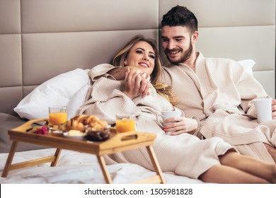 Young Happy Couple Having Breakfast In Luxury Hotel Room, Watching TV.