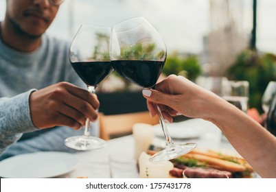 Young Happy Couple Having Date Dinner Celebrating Outdoors Making Cheers With Red Wine Glasses, People Enjoying Food Drink , Multiracial Couple Having Romantic Dinner At Outdoor Restaurant Terrace