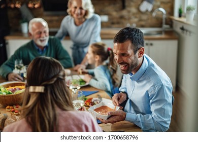 Young Happy Couple Having Family Lunch In Dining Room. Focus Is On Man Passing Food To His Wife. 