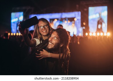 Young happy couple having fun and taking selfie with a smartphone at music festival. Young and cheerful couple on a music festival. - Powered by Shutterstock