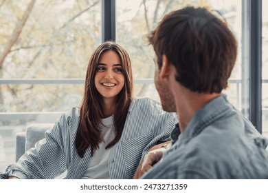 Young happy couple having fun talking laughing relaxing at home on couch, boyfriend embracing girlfriend telling funny joke sitting on sofa, humor in relationships, enjoying weekend together - Powered by Shutterstock