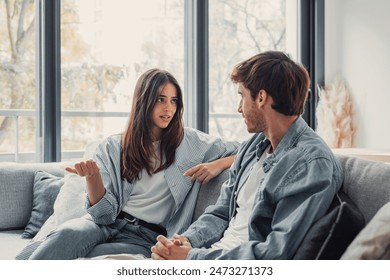 Young happy couple having fun talking laughing relaxing at home on couch, boyfriend embracing girlfriend telling funny joke sitting on sofa, humor in relationships, enjoying weekend together - Powered by Shutterstock