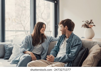 Young happy couple having fun talking laughing relaxing at home on couch, boyfriend embracing girlfriend telling funny joke sitting on sofa, humor in relationships, enjoying weekend together