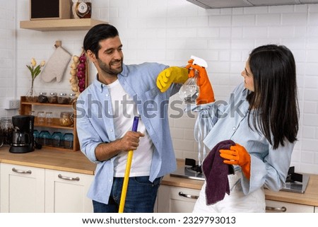 Young happy couple having fun while doing cleaning kitchen, They hold a mops and rags with spray bottle in hands and happily teasing each other, Happy family concept