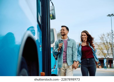 Young happy couple holding hands while getting in a bus at the station.