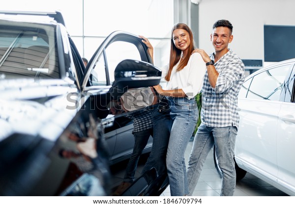Young\
happy couple just bought a new car in a\
dealership
