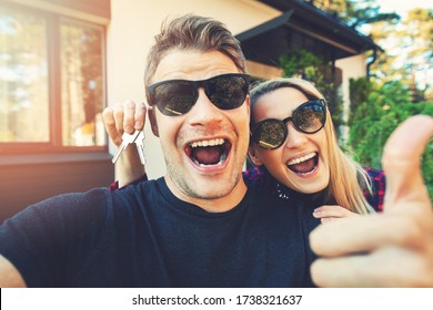 young happy couple with keys in hand standing outside of their new home and take a selfie - Powered by Shutterstock