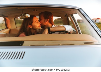 Young happy couple kissing while sitting together inside a car. Front window view