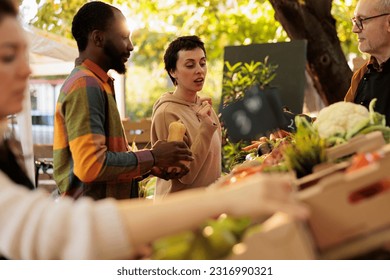 Young happy couple looking at farmers market eco produce and buying organic locally grown veggies. Senior farmer selling natural fruits and vegetables, having healthy bio products on stand.