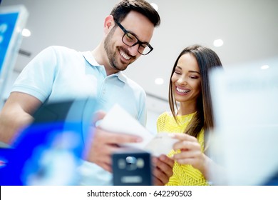 Young Happy Couple Looking At The Product Brochure At Technology Store.