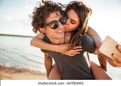 Young happy couple in love kissing and making selfie at the beach, piggyback ride