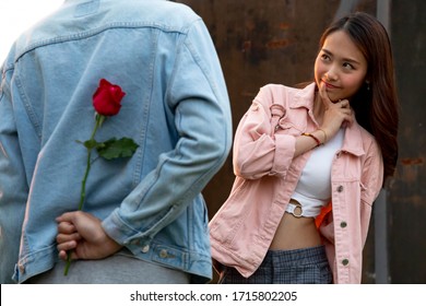 Young Happy Couple Love And Romantic At First Date Relationship. Asian Teenage Woman Surprise And Smiling At Boyfriend Gives Red Rose Flowers At Dinner In Valentine Day. Couple And Happiness Concept.