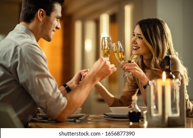 Young happy couple in love toasting with champagne while holding hands at dining table. Focus is on woman.  - Powered by Shutterstock