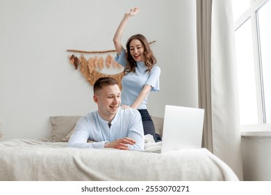 young happy couple in love use a laptop and rejoice in victory and success online on the bed at home, the woman sits on the man and celebrates good luck on the Internet - Powered by Shutterstock