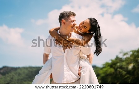 Young happy couple man and woman in white clothes on beach portrait, Girlfriend getting piggyback ride from boyfriend at sunrise over sea beach ocean outdoor in summer day