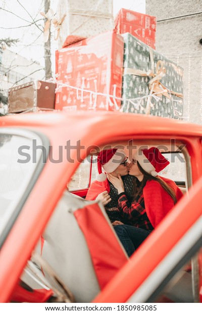Young happy couple man and woman in love in
Christmas hats hugging and sitting in a red retro car with New
Year's gifts. Kiss, girl, happiness, quarantine Christmas
celebration, holiday,
coronavirus.