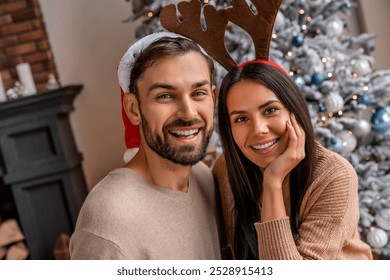 Young happy couple on Christmas day standing in front of the decorated tree on their living room. New Year celebration of young couple spouses husband and wife at home - Powered by Shutterstock