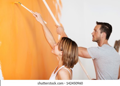 Young Happy Couple Painting Wall At New Home In Orange
