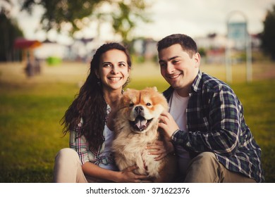 Young Happy Couple Playing With A Dog Chow Chow