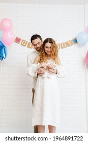 Young happy couple posing with baby shoes during gender reveal party indoors