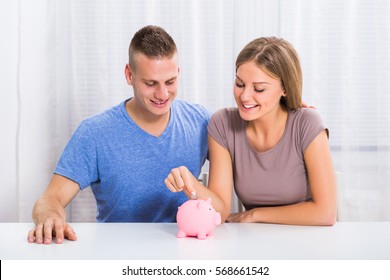 Young Happy Couple Putting Coin Into Piggy Bank.Money Saving For Happy Couple
