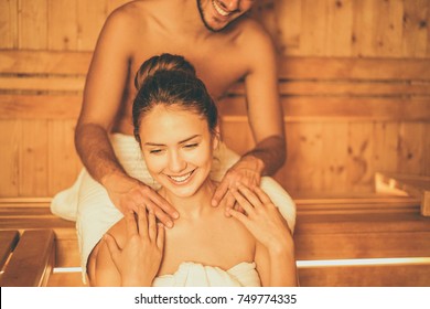 Young Happy Couple Relaxing Inside A Sauna At Spa Resort Hotel Luxury - Romantic Lovers Having A Bodycare Day In Steam Bath Man Making A Massage For His Girlfriend - Relax, Love, Lifestyle Concept