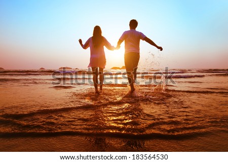 young happy couple running to the sea at sunset beach