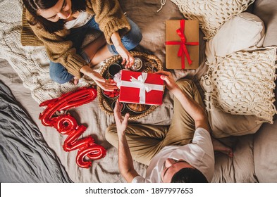 Young Happy Couple Sitting On Blankets In Bed At Home And Giving Presents In Boxes Over Breakfast And Sign Love On Bed, Top View. Saint Valentines Day Concept