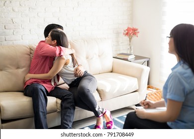 Young happy couple sitting on sofa embracing after successful therapy session with family psychologist